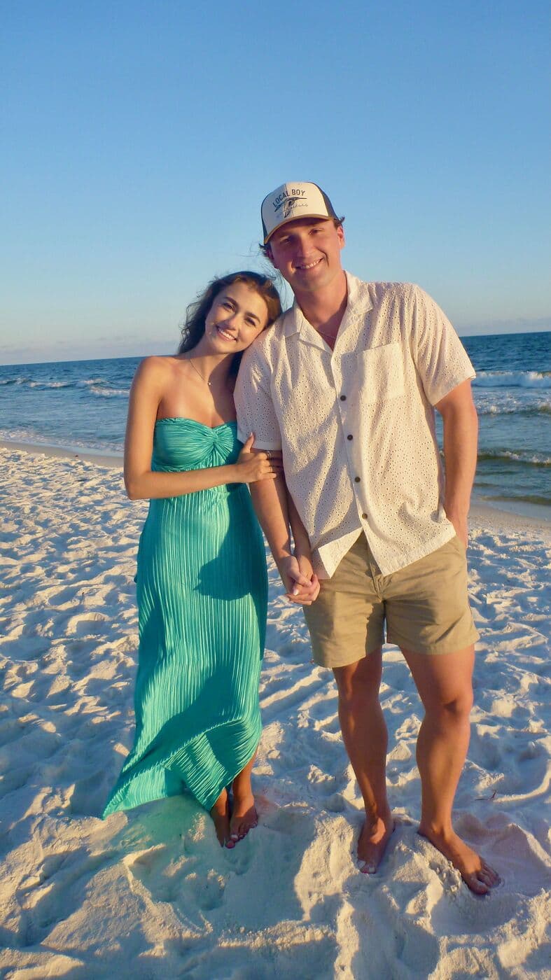 Elise in a green dress holding Tyler's hand at the water's edge