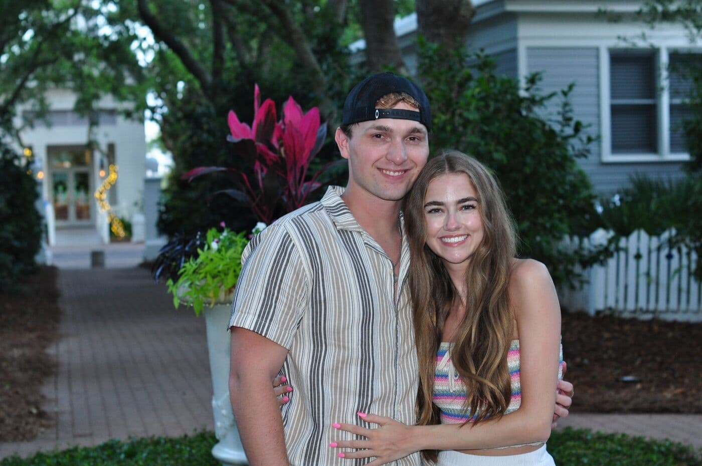 Elise and Tyler outside a white cottage with pink flowers