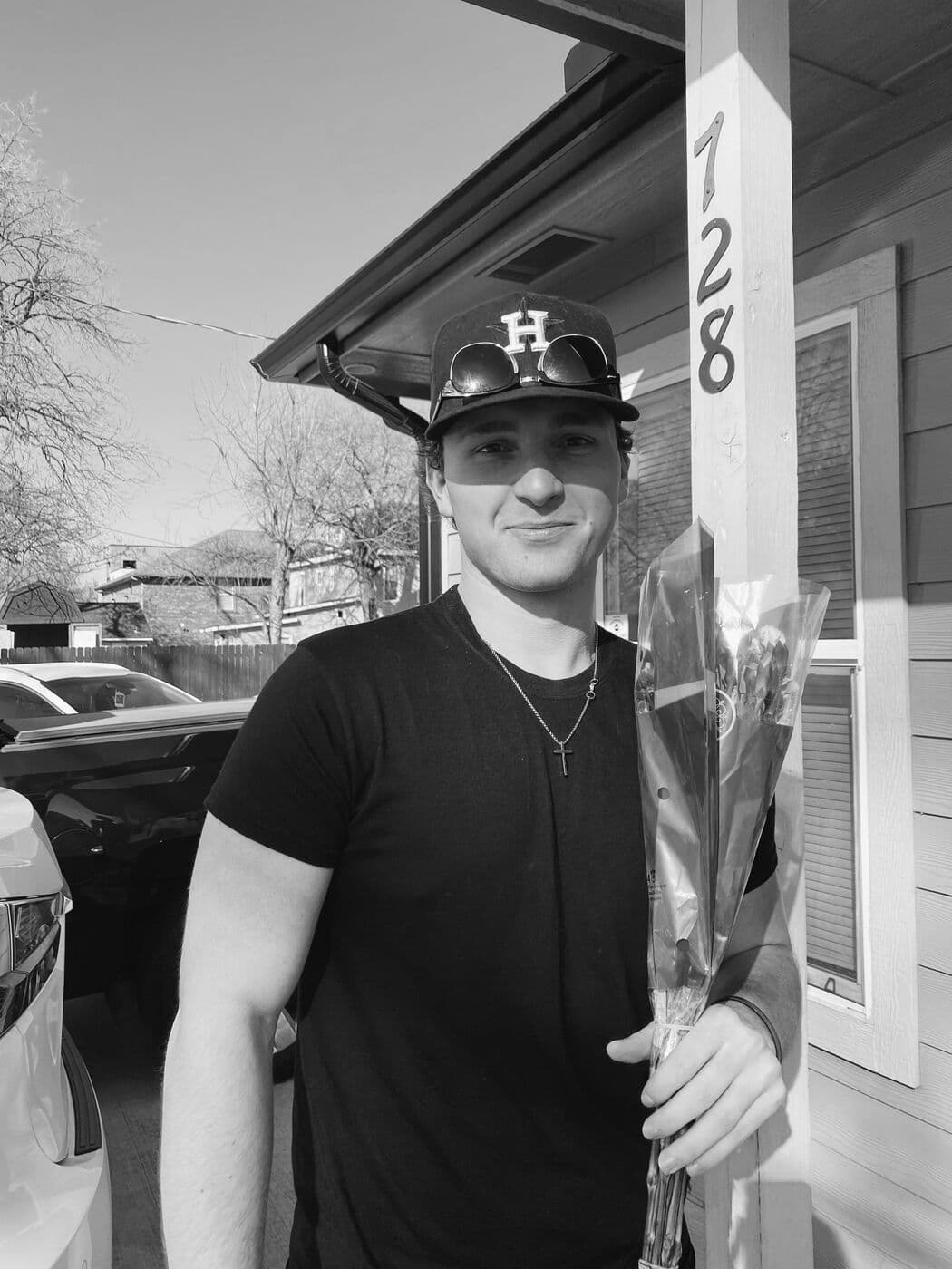Tyler on the porch holding a bunch of flowers, in black and white